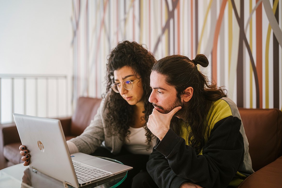 Zwei Studierende schauen konzertiert auf einen Laptop 