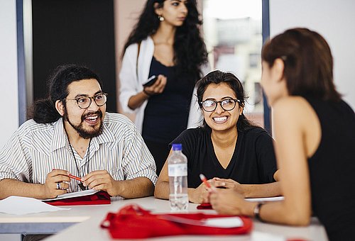 Drei Studierende des Master of Arts Studiengangs Gestión de Conflictos Interculturales sitzen an einem Tisch und unterhalten sich.
