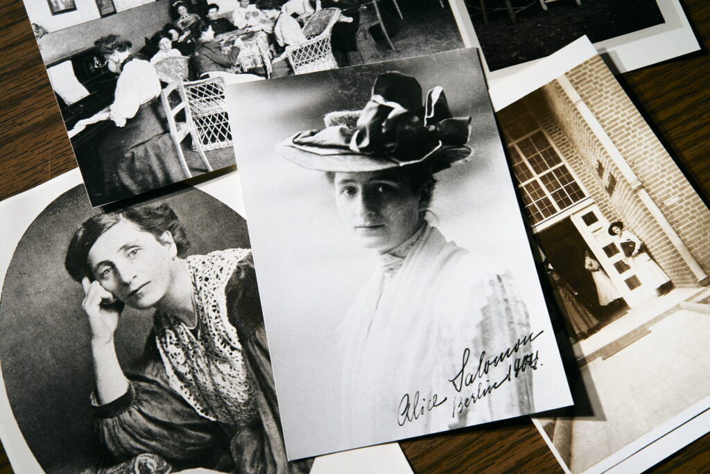 Mehrere schwarz-weiß Fotografien von Alice Salomon liegen lose übereinander auf einem Holztisch.