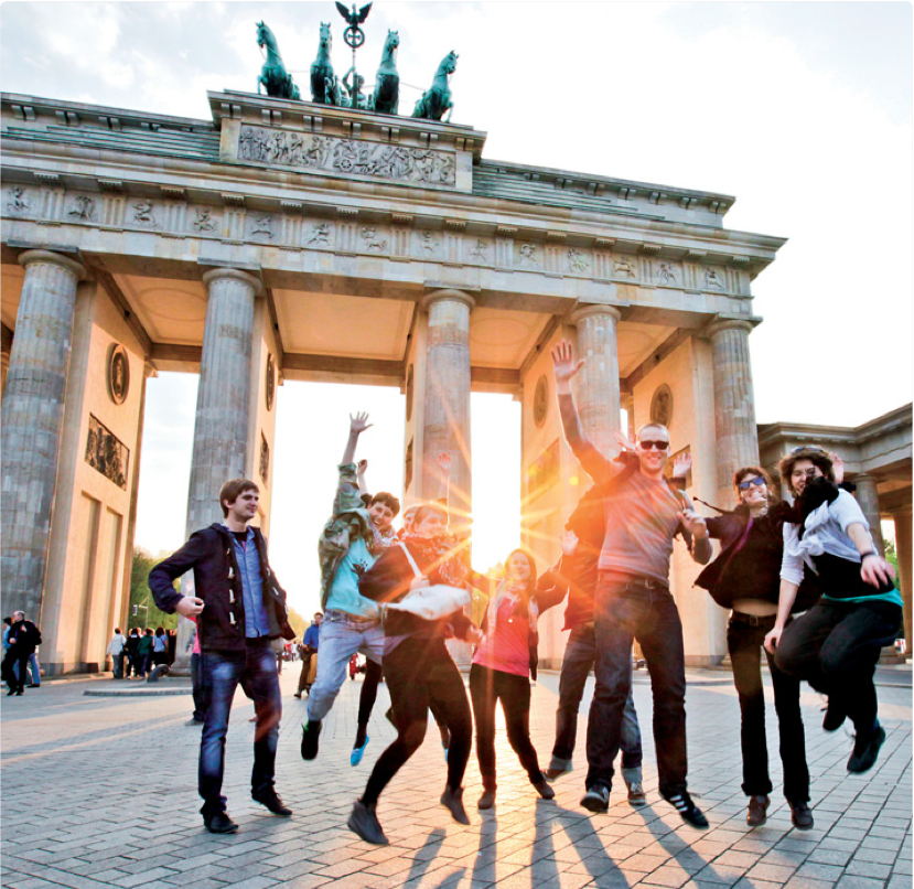 Vor dem Berliner Panorama des Brandenburger Tors springt eine Gruppe Studierender in die Luft.