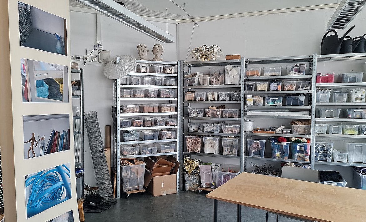 Zu sehen sind Materialregale sowie ein Arbeitstisch mit Holzplatte.