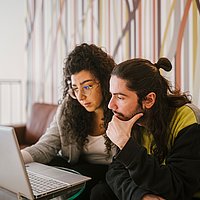 Zwei Personen sitzen vor einem Laptop