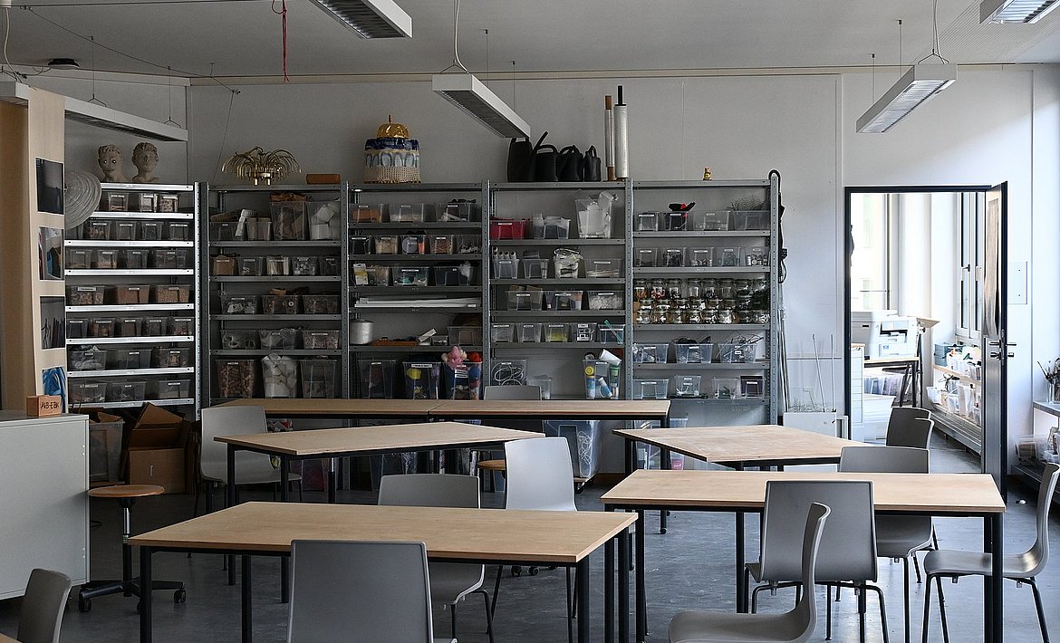 Es sind Tische im Werkstattraum vor dem Hintergrund der Materialregale zu sehen.