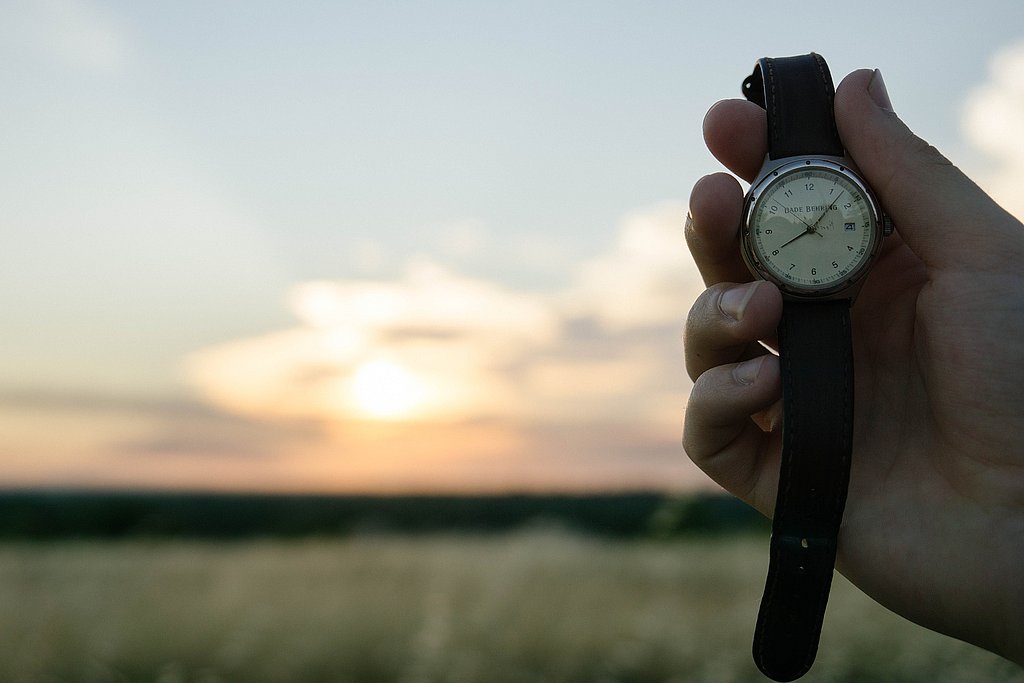 Blick auf Feld bei Sonnenuntergang, davor eine Armbanduhr