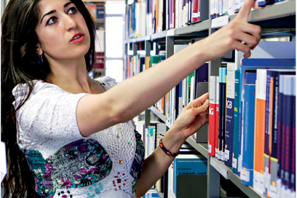 Eine Studentin nimmt in der Bibliothek ein Buch aus einem Regal