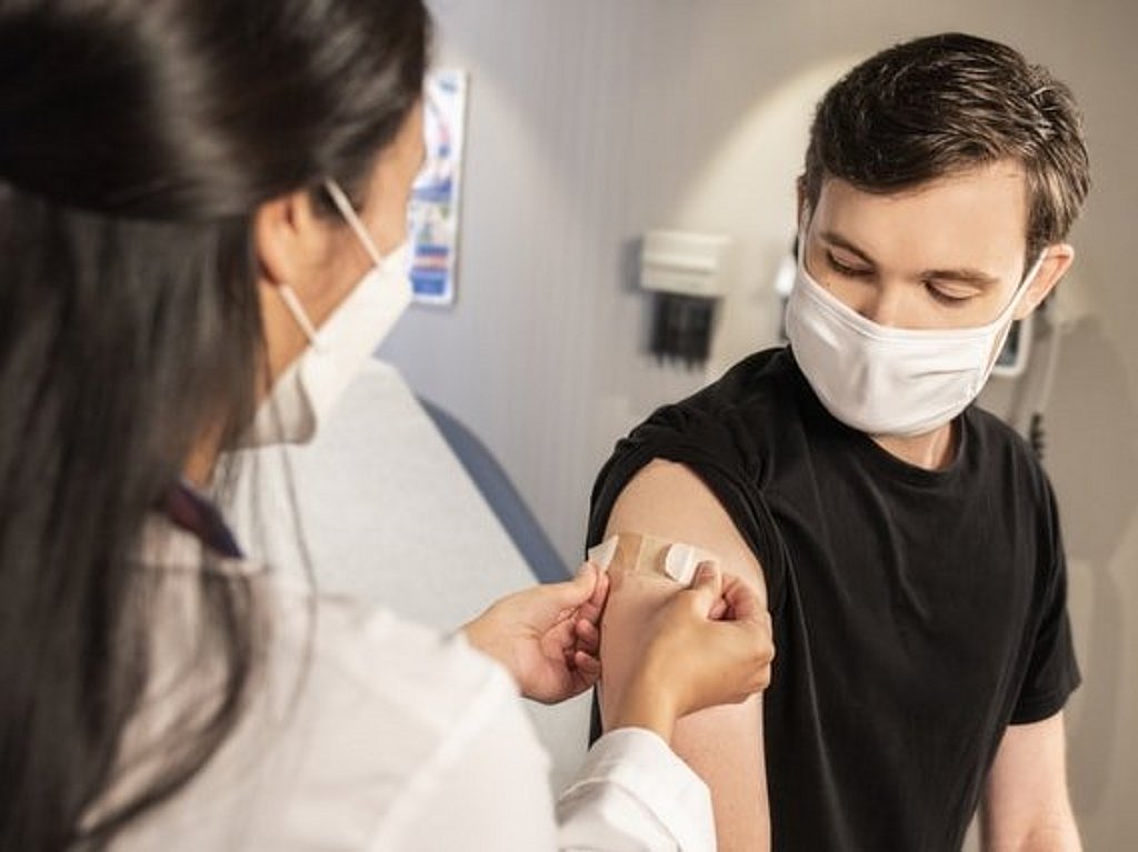 In einer klinischen Umgebung legt ein Gesundheitsdienstleister einen Verband auf die Injektionsstelle eines Patienten.