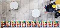 Wort "Empowerment" auf dem Boden in der Mensa. Jemand sitzt und isst