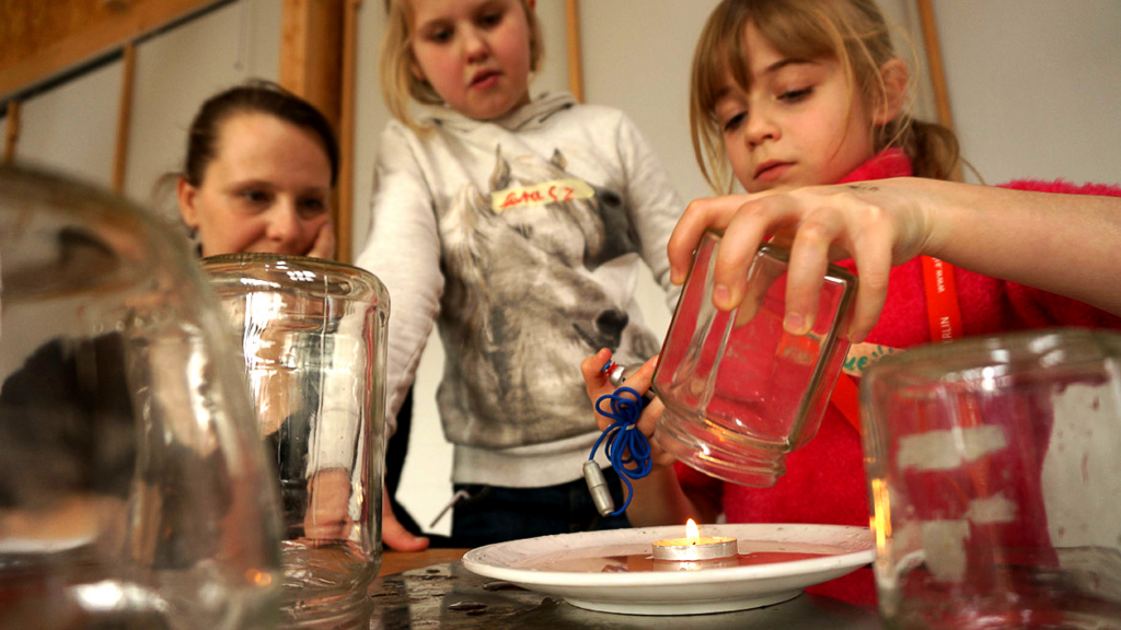 Zwei Kinder experimentieren mit einer Kerze und einem Glas.