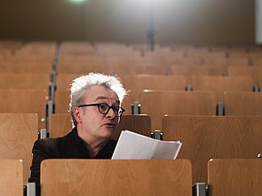 Guido Rademacher von hinter erleuchtet in einem leeren Hörsaal bei Verlesung der Jurybegründung