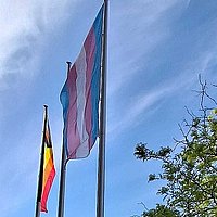 Die Progress Pride und die Trans Flag werden an den Fahnenmasten vor der ASH Berlin hochgezogen.