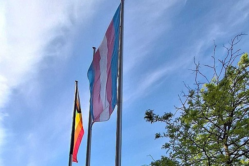 Die Progress Pride und die Trans Flag werden an den Fahnenmasten vor der ASH Berlin hochgezogen.