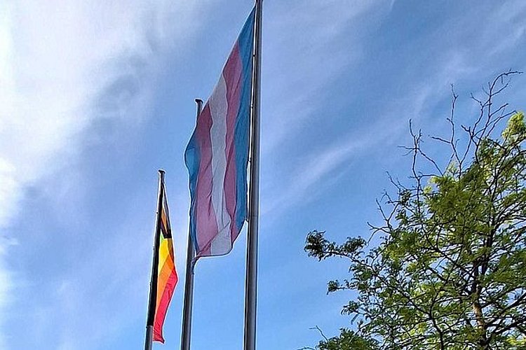 Die Progress Pride und die Trans Flag werden an den Fahnenmasten vor der ASH Berlin hochgezogen.