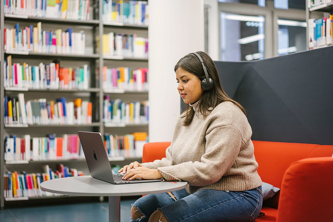 Eine Studierende sitzt mit Kopfhörern vor ihrem Laptop in der Bibliothek