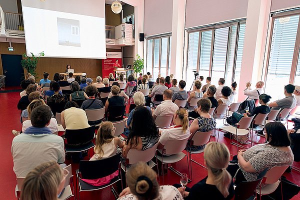 Das Publikum der Preisverleihung, fotografiert von hinten. Auch zu sehen ist die Bühne des Audimax. 