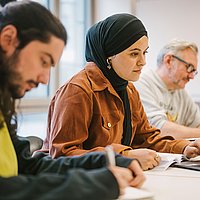 Drei Studierende der Alice Salomon Hochschule Berlin im Studiengang Soziale Arbeit sitzen in einem Seminarraum und arbeiten.