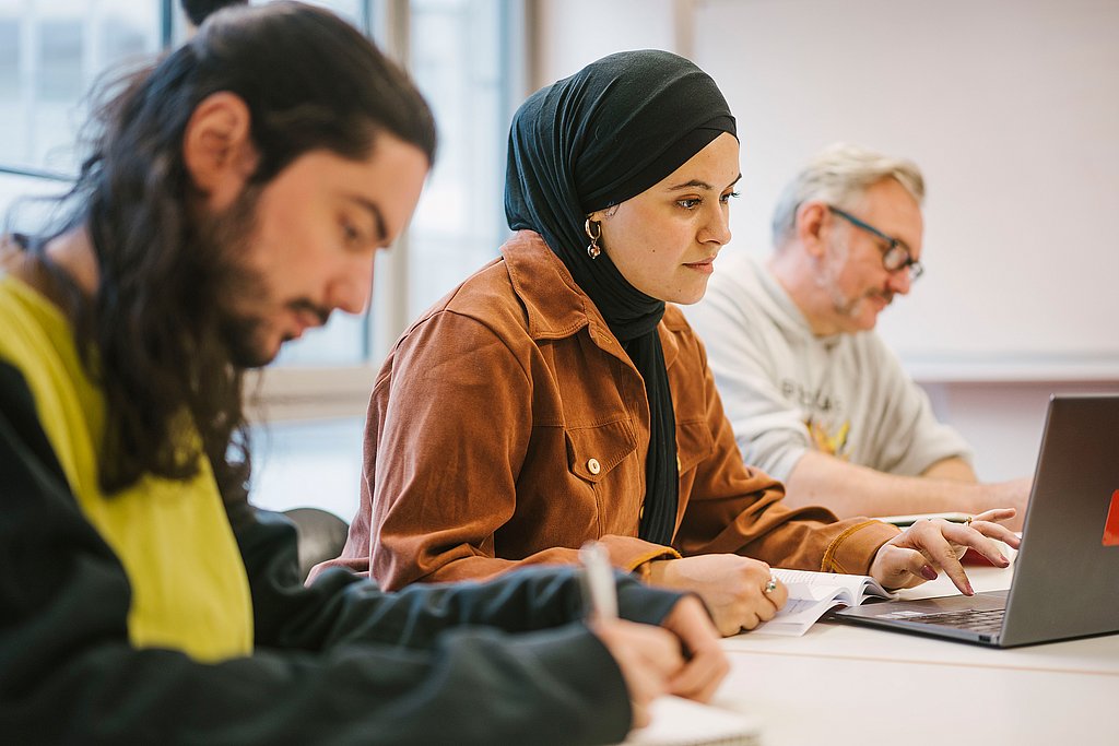 Drei Studierende der Alice Salomon Hochschule Berlin im Studiengang Soziale Arbeit sitzen in einem Seminarraum und arbeiten.
