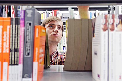 Blick durch ein Bücherregal: Ein Student sucht ein bestimmtes Buch.