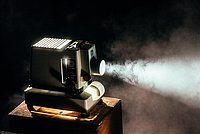 Ein laufender Filmprojektor auf einer Holzkommode, dunkler Raum.