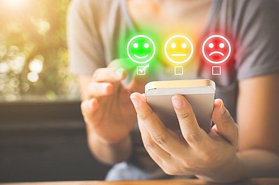 Person hält Smartphone in der Hand. Über dem Telefon leuchten drei bunte Smileys.