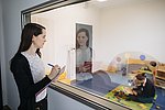 Eine Wissenschaftlerin beobachtet durch einen Einwegspiegel die Interaktion eines Kleinkindes mit seiner Mutter. 
