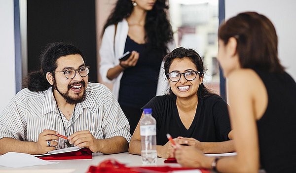 Drei Studierende des Master of Arts Studiengangs Gestión de Conflictos Interculturales sitzen an einem Tisch und unterhalten sich.