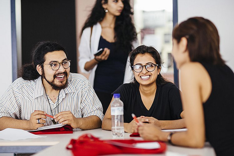 Drei Studierende des Master of Arts Studiengangs Gestión de Conflictos Interculturales sitzen an einem Tisch und unterhalten sich.
