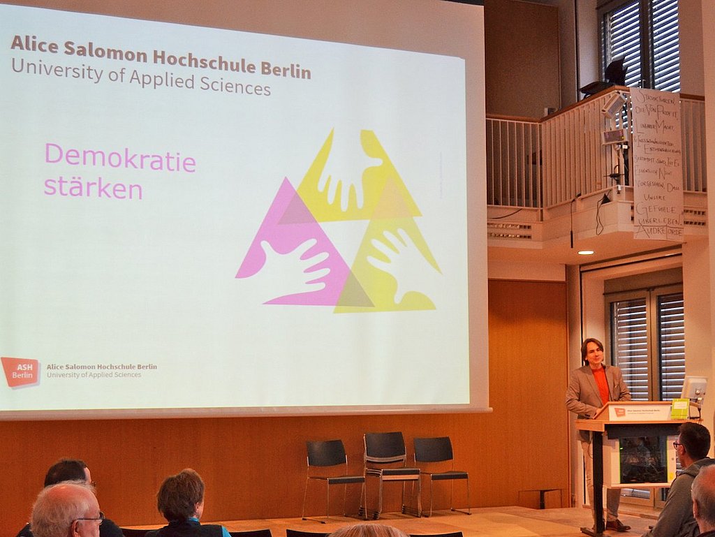 Begrüßung im Audimax der ASH, auf der Leinwand der Satz "Demokratie stärken", am Rednerpult Prof. Dr. Michael Brodowski