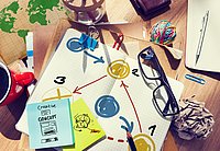 Blick auf einen Schreibtisch, im Fokus liegt eine selbst gemalte Grafik, die verschiedene Punkte zeigt, die mit Linien miteinander verbunden sind. Auf einem Zettel daneben steht "Creative Concept".