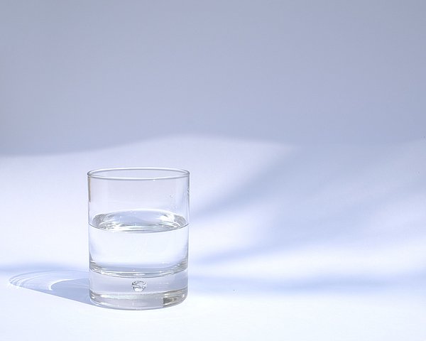 filled glas with water in front of a white wall