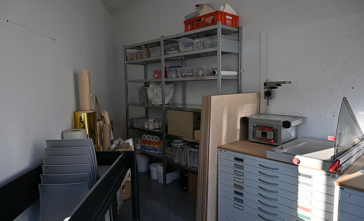 Es ist sind Papierschränke, ein Papierrollenvorrat sowie Lagerplatz der Werkstatt zu sehen.