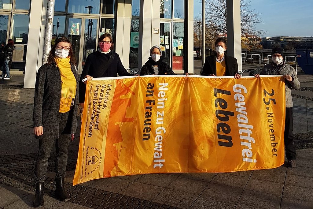 Auf dem Bild sind zu sehen Josephine Bürgel (Frauen*beauftragte ASH Berlin), Maja Loeffler (Gleichstellungsbeauftragte des Bezirks Marzahn-Hellersdorf), Elène Misbach (Mitarbeiterin ASH Berlin), Bettina Völter (Rektorin ASH Berlin) und Carola Kirschner (Leiterin Frauenzentrum Matilde e.V.). Gemeinsam halten sie die Fahne „Gewaltfrei Leben. Nein zu Gewalt an Frauen“.