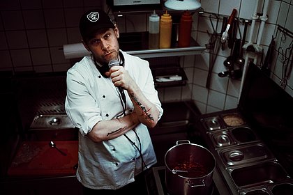 Paul Denkhaus mit Kochkittel und Mikro in einer Küche