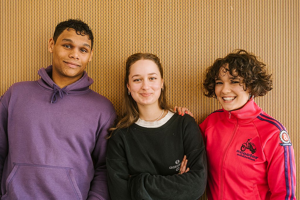 Drei Studierende lachen in die Kamera