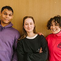 Drei Studierende lachen in die Kamera