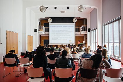 Blick von hinten in das Audimax (großer Vorlesesaal), Vorlesung einer Professorin vor ca. 50 Studierenden