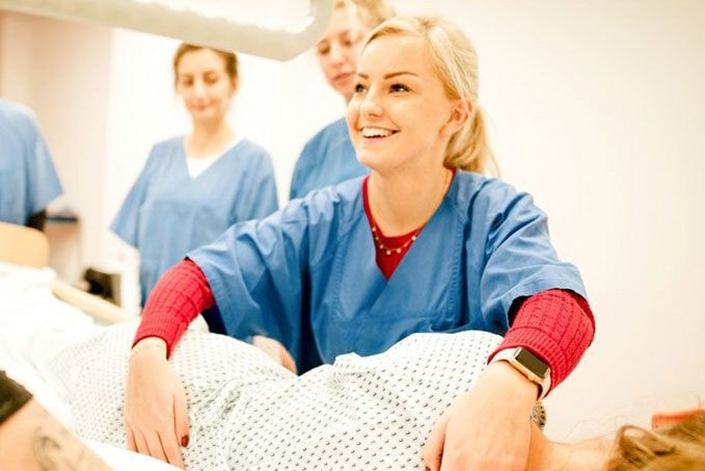Vier Personen beim Arbeiten in der Pflege wobei eine Frau im Vordergrund eine Patientin lagert