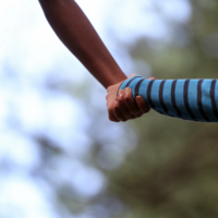 Detailaufnahme: eine Erwachsene Person und ein Kind laufen Hand in Hand, es sind nur die Arme und Hände der beiden erkennbar