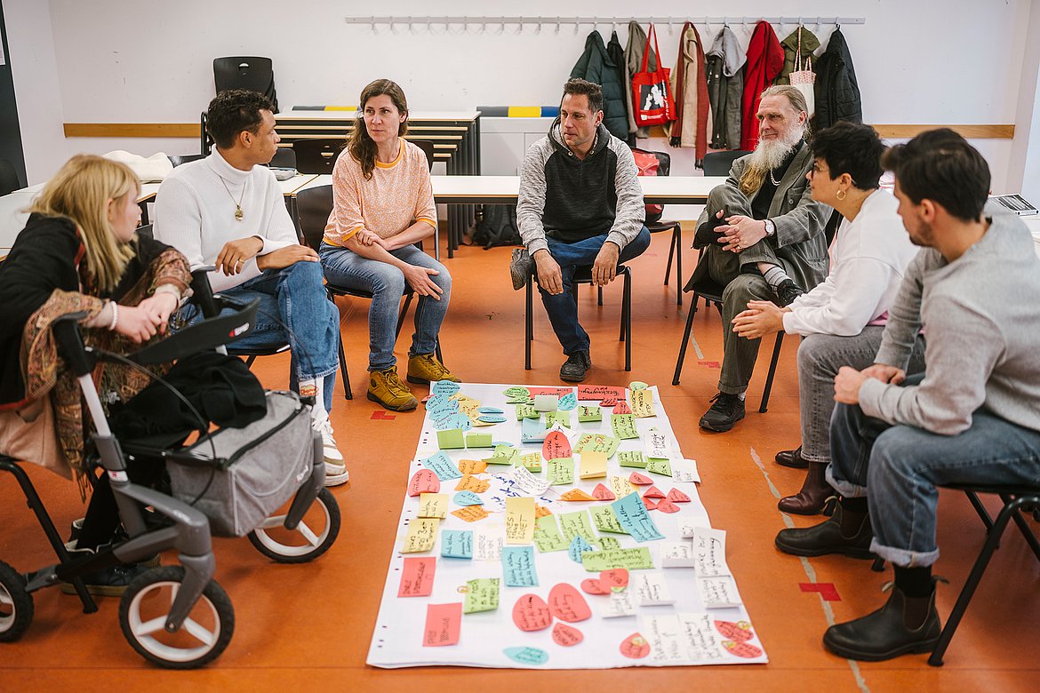 Eine Studierendengruppe, die auf dem Boden im Kreis sitzt und an einem Thema arbeitet.