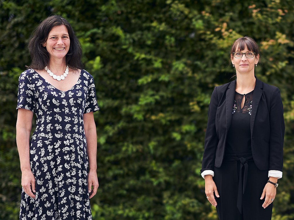 Bettina Völter und Jana Einsporn stehen vor einer grünen Hecke und schauen in die Kamera