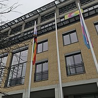 Foto vom Hauptgebäude der ASH Berlin und den Trans*- und Progress-Flaggen, die an den Fahnenmasten hängen.