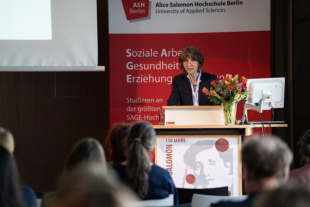 Aleida Assmann steht hinter einem Rednerpult und spricht ins Mikrofon