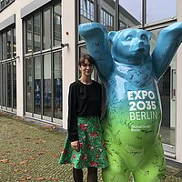 Auf dem Foto ist der Expo-Bär zu sehen, der im Innenhof der ASH Berlin steht. Die ASH-Kanzlerin Jana Einsporn steht neben dem Bären.