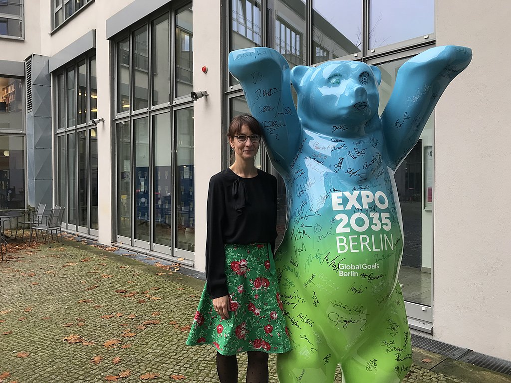 Auf dem Foto ist der Expo-Bär zu sehen, der im Innenhof der ASH Berlin steht. Die ASH-Kanzlerin Jana Einsporn steht neben dem Bären.