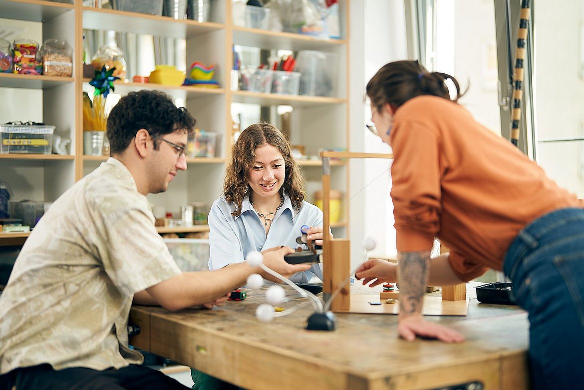 Drei Studierende der ASH Berlin sitzen in der Lernwerkstatt der Hochschule an einem Tisch und führen Experimente durch.