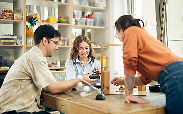 Drei Studierende der ASH Berlin sitzen in der Lernwerkstatt der Hochschule an einem Tisch und führen Experimente durch.