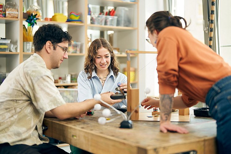 Drei Studierende der ASH Berlin sitzen in der Lernwerkstatt der Hochschule an einem Tisch und führen Experimente durch.