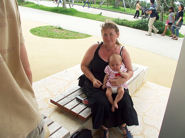Angelika Weirauch sitzt auf einer Bank neben einem Spielplatz und hält ihre Tochter im Arm.
