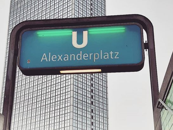 Einggansschild des U-Bahnhofes Alexanderplatz, aufgenommen mit Blick von unten, im Hintergrund ein Hochhaus