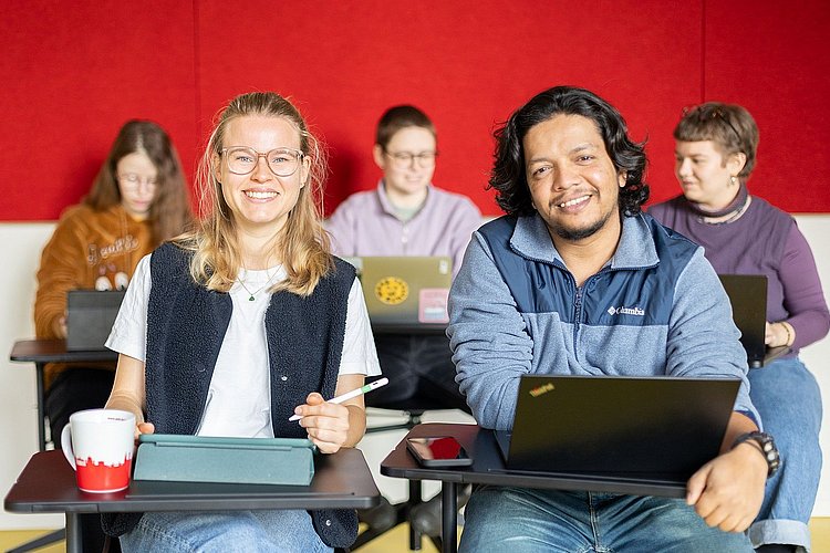 Fünf Studierende sitzen in einem Seminar der ASH Berlin. Zwei Studierende schauen lächelnd in die Kamera. 