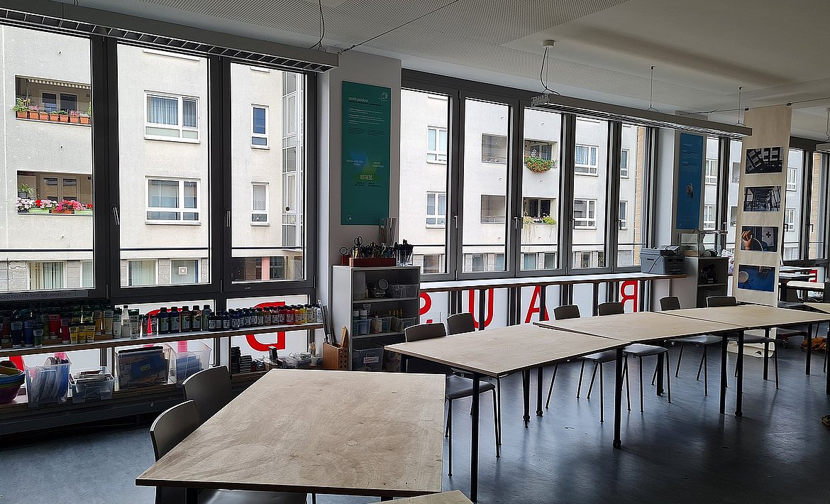 Es sind mehrere Arbeitstische vor der Fensterfront der Werkstatt zu sehen.